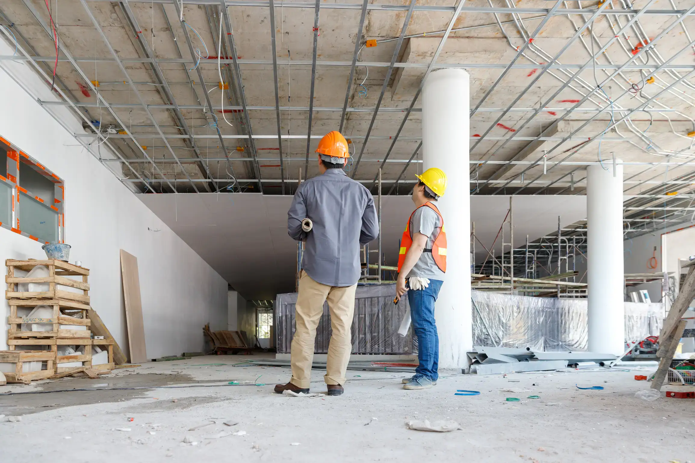 ALT: Zwei Bauarbeiter mit Helm auf einer Baustelle bei der Inspektion der Deckeninstallation.