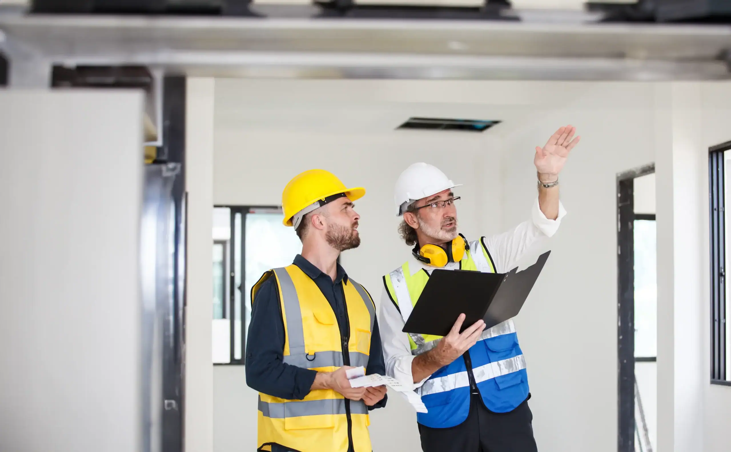 Männer in Sicherheitshelmen und Warnwesten bei Bauarbeit im Innenraum.